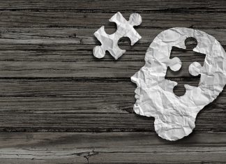 Mental health symbol Puzzle and head brain concept as a human face profile made from crumpled white paper with a jigsaw piece cut out on a rustic old double page spread horizontal wood background.